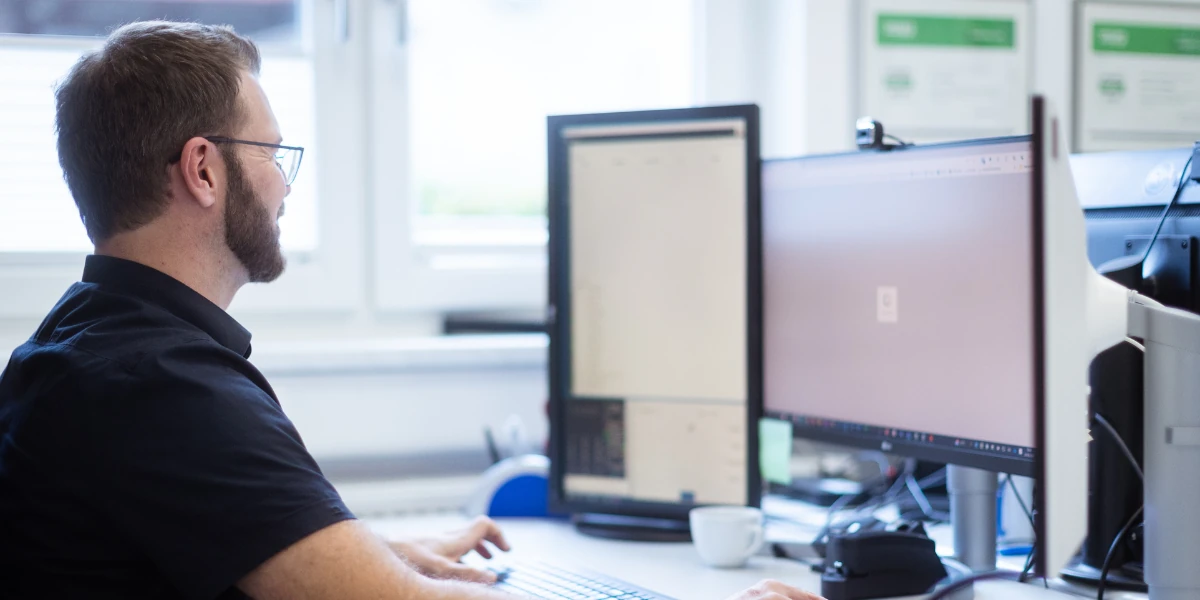 Mann mit Brille arbeitet am PC mit zwei Monitoren im Büro am Schreibtisch